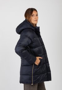 Giacca puffa blu navy con cappuccio, caratterizzata da un design trapuntato, tasche con zip frontali e una texture lucida e liscia.