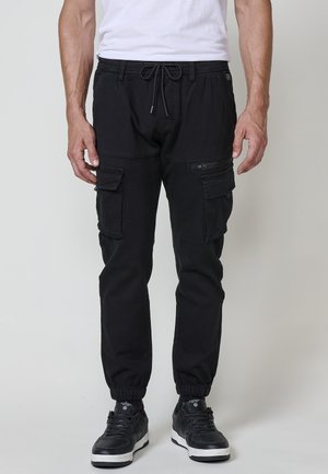 Pantalons cargo noirs avec taille et poignets élastiques, équipés de poches latérales et d'un cordon de serrage. Le tissu semble durable et léger.
