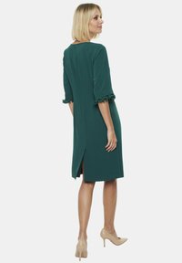 Zielona sukienka do kolan z rękawami o długości trzech ćwierć. Posiada rozcięcie z tyłu oraz zapięcie na guziczek w okolicy szyi. Gładki materiał.
