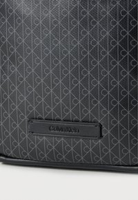 Μαύρη δερμάτινη τσάντα με γεωμετρικό μοτίβο που επαναλαμβάνει το λογότυπο «CK», υφή στην επιφάνεια και ορθογώνια ετικέτα με ανάγλυφο το όνομα «Calvin Klein».