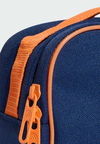 Granatowa torba z tkaniny z pomarańczowym zamkiem błyskawicznym i paskiem, o gładkiej fakturze i wyraźnym przeszyciu wzdłuż krawędzi zamka.