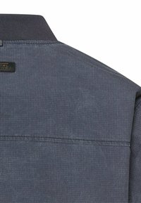 Nahaufnahme des Rückens einer dunkelblauen, strukturierten Jacke mit einem schwarzen, gerippten Kragen und einer sichtbaren Naht über den Schulterblättern.