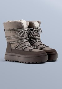 Szare ocieplane zimowe buty z wysoką cholewką, zaokrąglonym noskiem i grubą gumową podeszwą. Sznurowadła i miękka wyściółka podkreślają ich design.