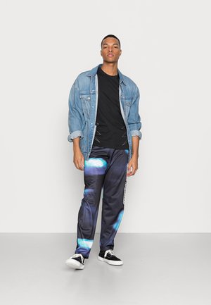 Denimjakke, sort t-shirt, mønstrede svedbukser med blå accenter og sorte sneakers. Slank, afslappet pasform med elastisk talje.