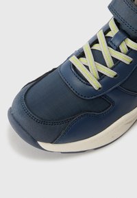Sneaker navy con tomaia in pelle e tessuto strutturato, punta rinforzata, suola chiara e lacci a contrasto verdi brillanti e grigi.