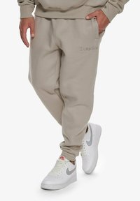 Beige tepláky vyrobené z bavlněné směsi, s elastickými manžetami a bočními kapsami. Vyšité logo "Dropsize" v přední části. Kombinujte s bílými teniskami.