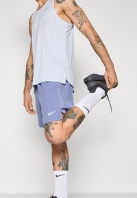 Débardeur de sport bleu clair avec fentes sur les côtés ; shorts lavande avec logo Nike blanc ; chaussettes blanches avec accents noirs ; chaussures noires.
