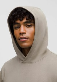 Hellbrauner Hoodie mit Rundhalsausschnitt und einer großen Kapuze. Der Stoff wirkt weich mit einer glatten Textur und minimalen Nähten.