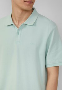 Lichtgroen gemêleerd polo shirt van gestructureerde stof. Beschikt over een klassieke kraag, een placket met twee knopen en subtiele logo borduursel op de borst.