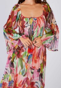 Floral dress in lightweight, sheer fabric with vibrant colors. Features a square neckline, smocked bodice, bell sleeves, and tassel accents.