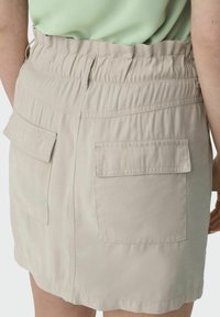 La falda beige de cintura elástica presenta una textura suave, dos bolsillos traseros y un diseño ajustado, que se extiende hasta la mitad del muslo.