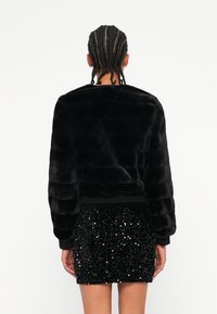 Crna faux fur jakna s teksturiranim, rebrastim dizajnom i dugim rukavima. Uparena s crnom mini suknjom od šljaštećih kamenčića koja ima uski kroj.