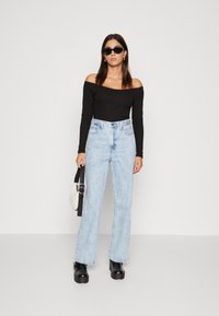 Haut noir à肩 revis, jean taille haute bleu clair, bottes à plateforme noires et petit sac à main blanc. Les accessoires comprennent des lunettes de soleil noires.