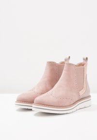 Pár světle růžových semišových Chelsea bot s elastickými bočními panely, poutky na patě a bílými gumovými podešvami s vroubkovanými okraji.