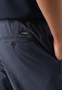 Marinblå shorts gjorda av lättviktsmaterial med elastisk midja. Har en bakficka med knäppning och Ecoalf-märke.