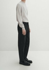 Pull en maille côtelée gris clair à manches longues associé à un pantalon noir ample et des chaussures noires à lacets. Design minimaliste, textures lisses.