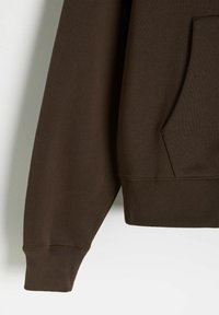 Brązowy sweter z ribbowanymi mankietami i dolnym wykończeniem, gładką teksturą i kieszenią z przodu, przedstawiony z boku, z widoczną częścią rękawa i dolnej części.