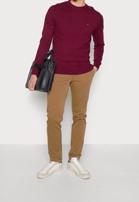 Burgundský svetr s kulatým výstřihem, khaki slim-fit kalhoty, bílé tenisky se šedými akcenty a černá kožená taška.