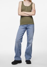 Olivgrön rippad linne med knapppdetaljer, matchad med ljusblå utsvängda jeans och svarta klumpiga skor.