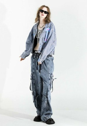 Chaqueta de mezclilla con textura desgastada, color azul claro, detalles de parches, pantalones cargo holgados a juego y zapatos negros gruesos. La silueta es de corte oversized.