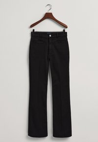 Pantalones de mezclilla negros colgados en un perchero de madera, con cierre de botón, bolsillos frontales y un diseño de pierna recta.