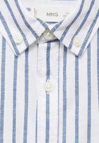 Valkoinen nappi-shirt jossa on siniset pystysuorat raidat, kauluksellinen kaula-aukko ja kaksi valkoista nappia kauluksessa. Rakenteellinen kangas.