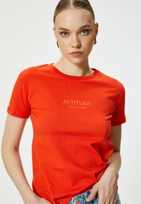 Camiseta de algodón roja con mangas cortas, cuello redondo y el texto "LA ACTITUD LO ES TODO" impreso en una fuente de contraste en la parte frontal.