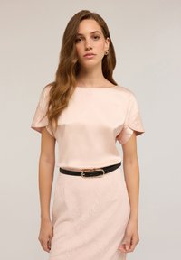 Blusa di raso rosa con maniche corte e scollatura a barca. Abbinata a una gonna a tubino in pizzo aderente e una cintura nera con dettagli in oro.