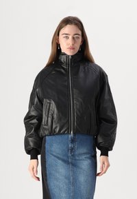 Veste bomber en cuir noir avec un col haut, fermeture éclair sur le devant et poches latérales, assortie d'une jupe en jean avec une couture centrale.