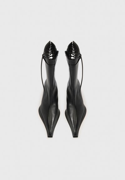 Μαύρα δερμάτινα μποτάκια με μυτερή μύτη, κομψό σχέδιο, ανοιχτή φτέρνα και λεπτομέρεια δέσιμου κορδονιού στο πάνω μέρος. Λείο υλικό με ματ φινίρισμα.