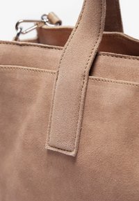 Borsa tote in suede beige chiaro con un manico largo e piatto e cuciture sottili lungo i lati. Texture liscia con una finitura morbida.