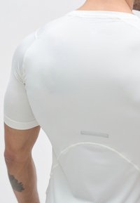 T-shirt de sport blanc ajusté à manches courtes, tissu texturé et bande réfléchissante à l'arrière. Les détails des coutures accentuent la silhouette.