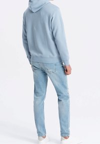 Ljusblå hoodie med ribbade muddar, ihopparad med ljusblå slitna jeans och vita sneakers, sedd bakifrån.