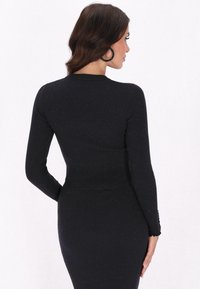 Abito lungo a maniche lunghe nero a coste con una silhouette aderente, caratterizzato da un tessuto texturizzato, un orlo ondulato e sottili accenti di brillantezza.