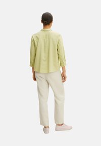 Camicia verde chiaro a maniche lunghe con colletto e piega posteriore, abbinata a pantaloni bianco sporco e sneakers rosa chiaro. Fit semplice e rilassato.