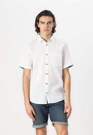 White short-sleeve shirt in lightweight fabric with a buttoned front, a chest pocket, and dark buttons; styled with rolled sleeves.