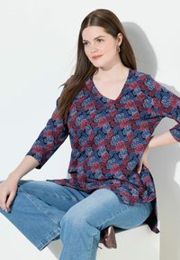 Marineblaues und rotes Blumenmuster-Tunikashirt mit Dreiviertelärmeln und V-Ausschnitt, kombiniert mit hellblauen weit geschnittenen Jeans. Glatte Stofftextur.