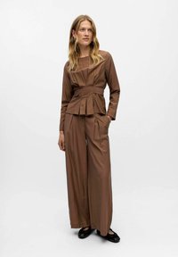 Brown two-piece outfit featuring a fitted long-sleeve top with pleats and wide-leg pants. Made from a smooth fabric with a matte finish.