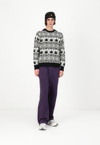Black and white sweater with leaf pattern, paired with loose purple sweatpants, black beanie, and gray athletic shoes.