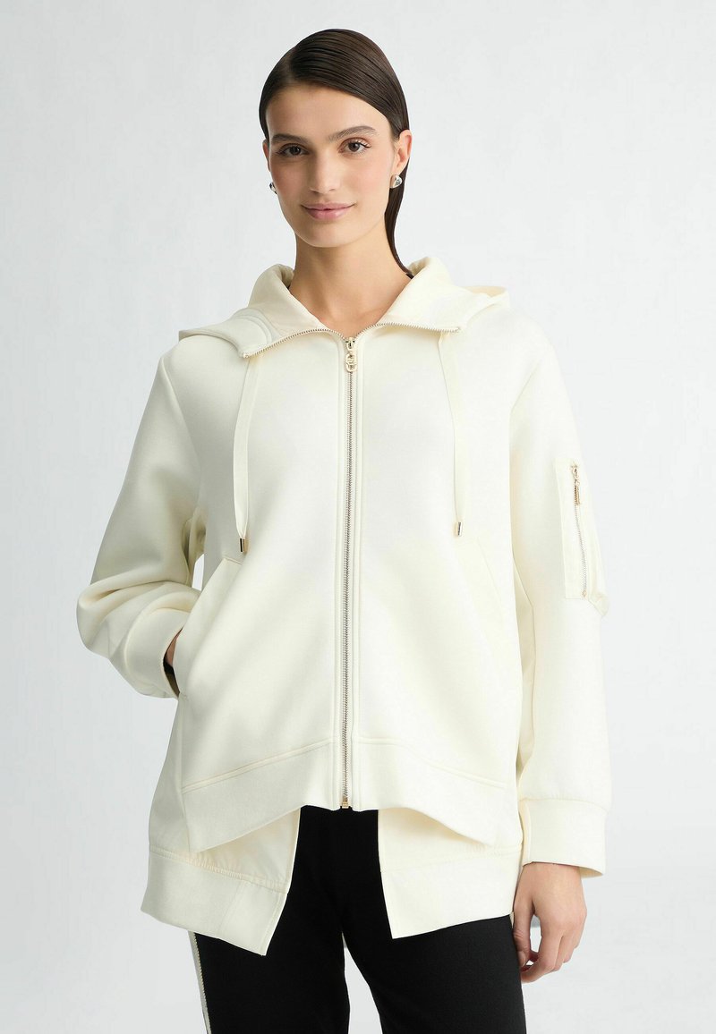 Witte zip-up hoodie met een grote capuchon, voorzakken en een zijzak met rits. Zachte textuur en een relaxte fit met een gesplitste zoom.