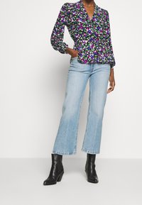 Blus med blommönster i lila, blått och vitt med puffärmar; kombinerad med ljusblå utsvängda jeans och svarta klackstövlar.