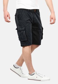 Black cargo shorts with multiple side pockets, a belt, and a relaxed fit, paired with white perforated sneakers.