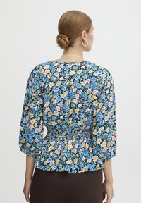 Blusa floreale nei toni del blu, rosa e giallo su sfondo nero, con maniche a palloncino e vita arricciata per una vestibilità aderente.
