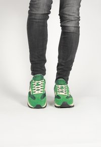 Zelené a krémové športové tenisky vyrobené z nubuku a kože, s polstrovanou podrážkou, šnurovacím dizajnom a textúrovanými akcentmi.