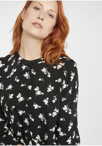 Schwarzes Hemdkleid mit floralem Druck, das weiße Blumen zeigt, lange Ärmel, einen runden Ausschnitt und einen weichen, strukturierten Stoff hat.