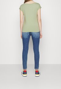 T-shirt vert à manches courtes associé à un jean bleu ajusté et des baskets multicolores. Le t-shirt possède un col large et une texture lisse.