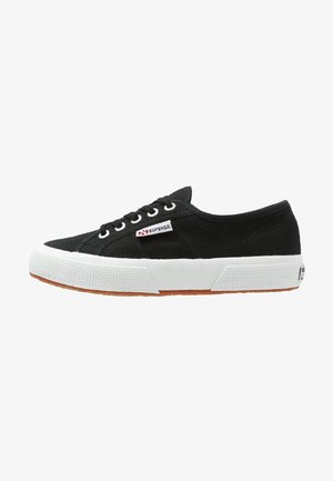 Sneaker nera in tela con suola e punta in gomma bianca, design con sei fori per i lacci e un piccolo logo rosso sul lato. Superficie texture.