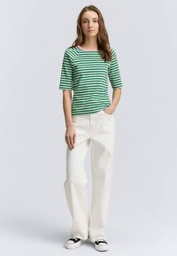 Žalias ir baltas dryžuotas trumpomis rankovėmis marškinėlius su rožine apykakle, derinamas su baltais plačiomis kelnėmis ir juodais sportbačiais.