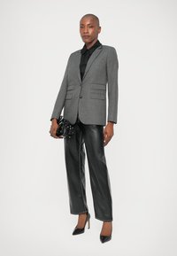 Blazer de espiga gris con solapas afiladas, combinado con pantalones de cuero negros y tacones puntiagudos. Llevando un pequeño bolso negro.