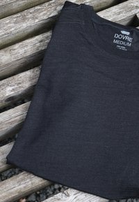 Mørkegrå uld t-shirt foldet på en træoverflade. Har en rund halsudskæring og rent, enkelt syning. Mærket synligt læser "Dovre Medium."